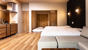 A modern hotel room with a wooden floor, a sofa bed, a wooden dresser, and a wall-mounted light fixture.