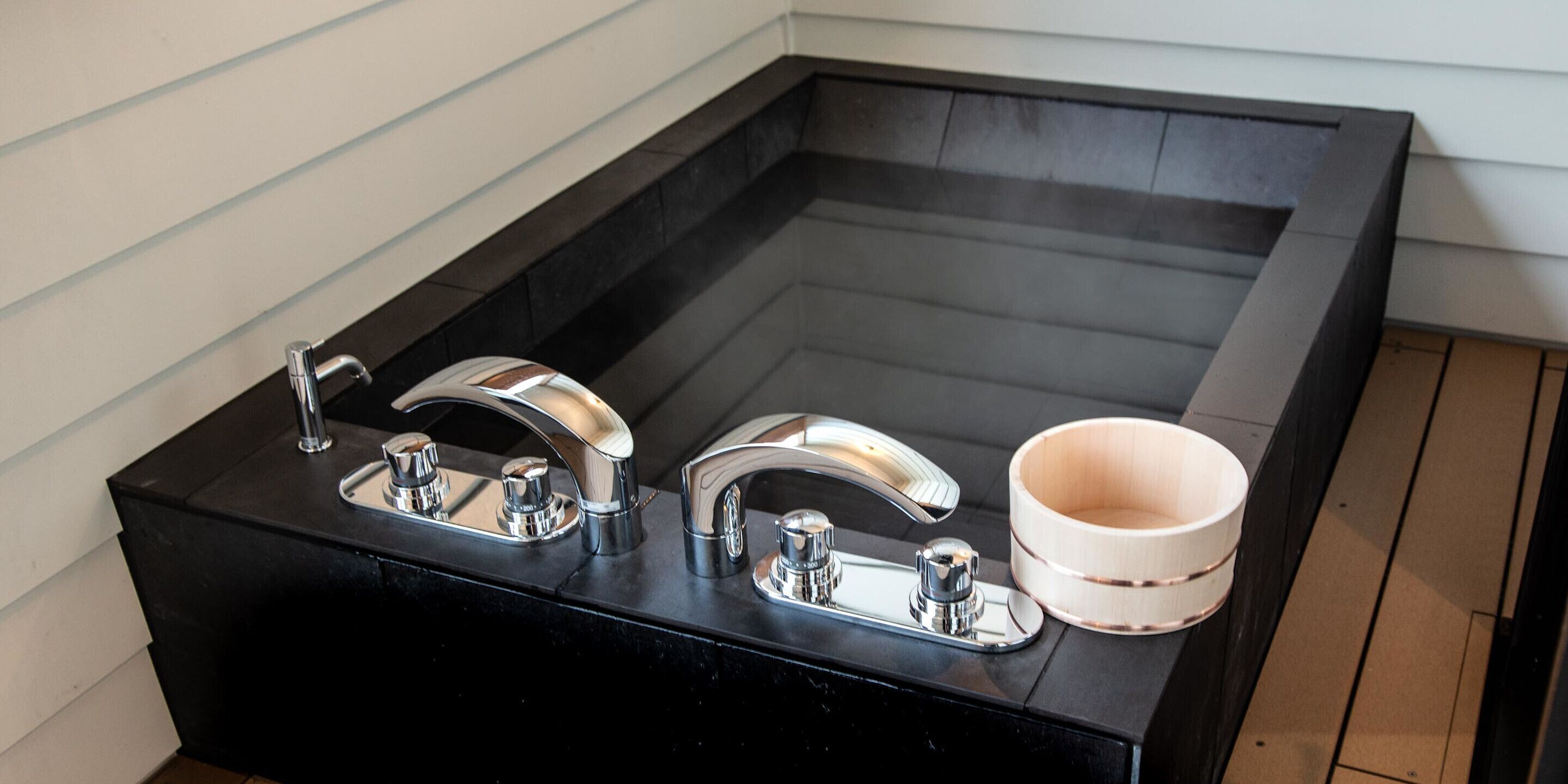 A black countertop with two chrome faucets and a wooden cup holder.