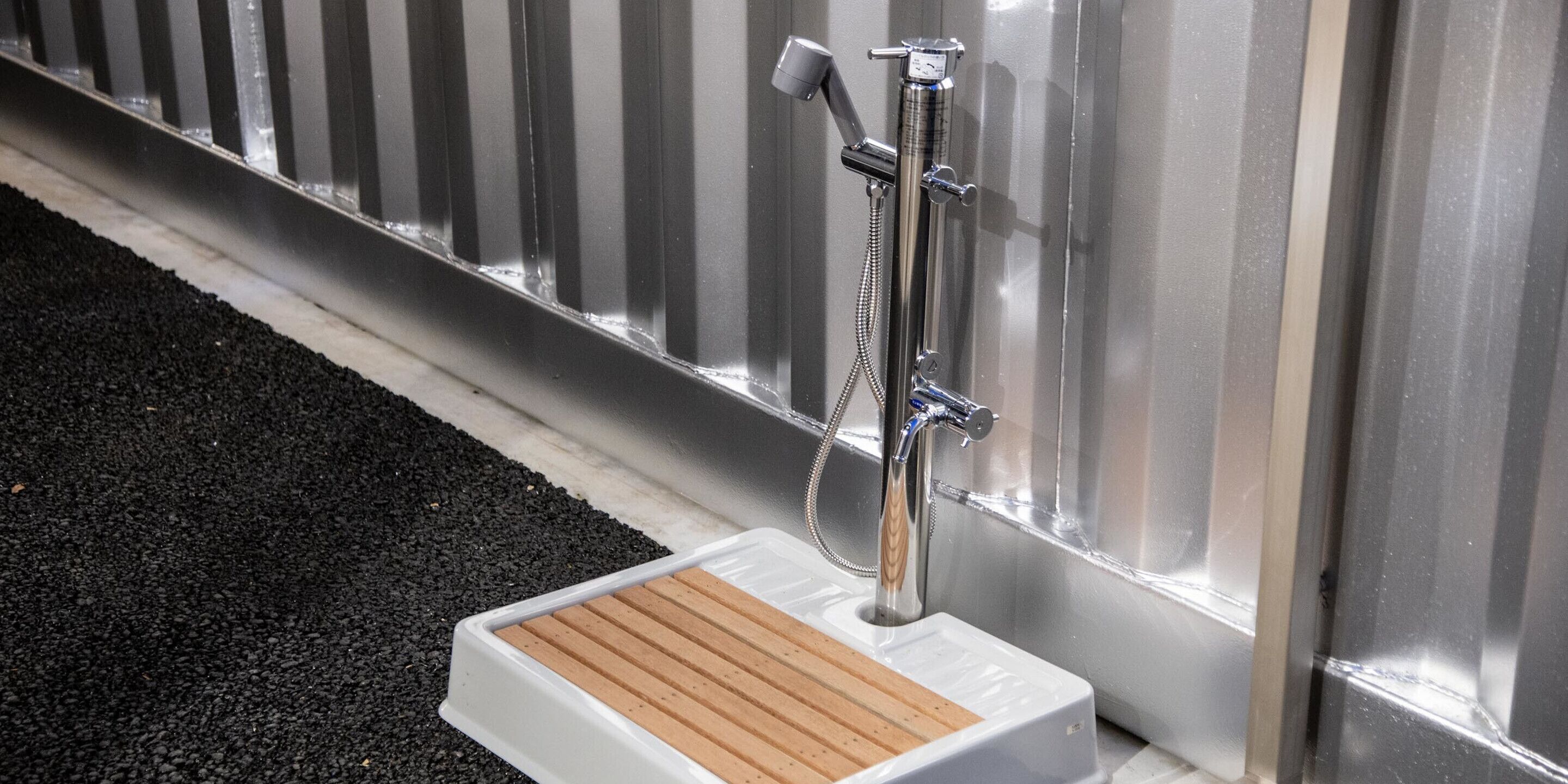 A portable shower unit with a wooden seat and chrome fixtures against a metallic wall.