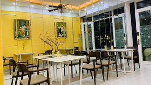 A dining area with yellow walls, mirrored partitions, and a ceiling fan. - Chez Mimosa Local Homestay (Ho Chi Minh City)