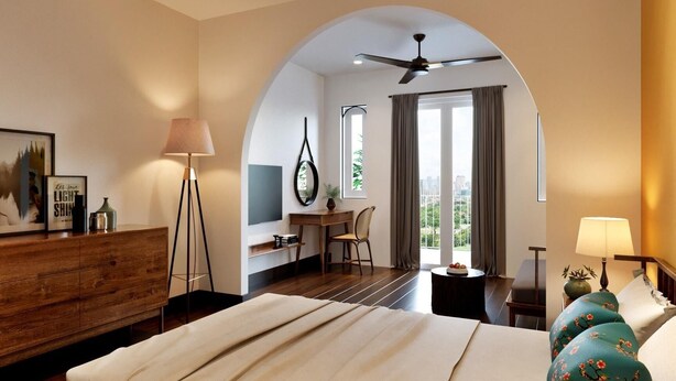 A hotel room with a bed, a desk, a chair, a lamp, and a view of the city through large windows. - Chez Mimosa Local Homestay (Ho Chi Minh City)