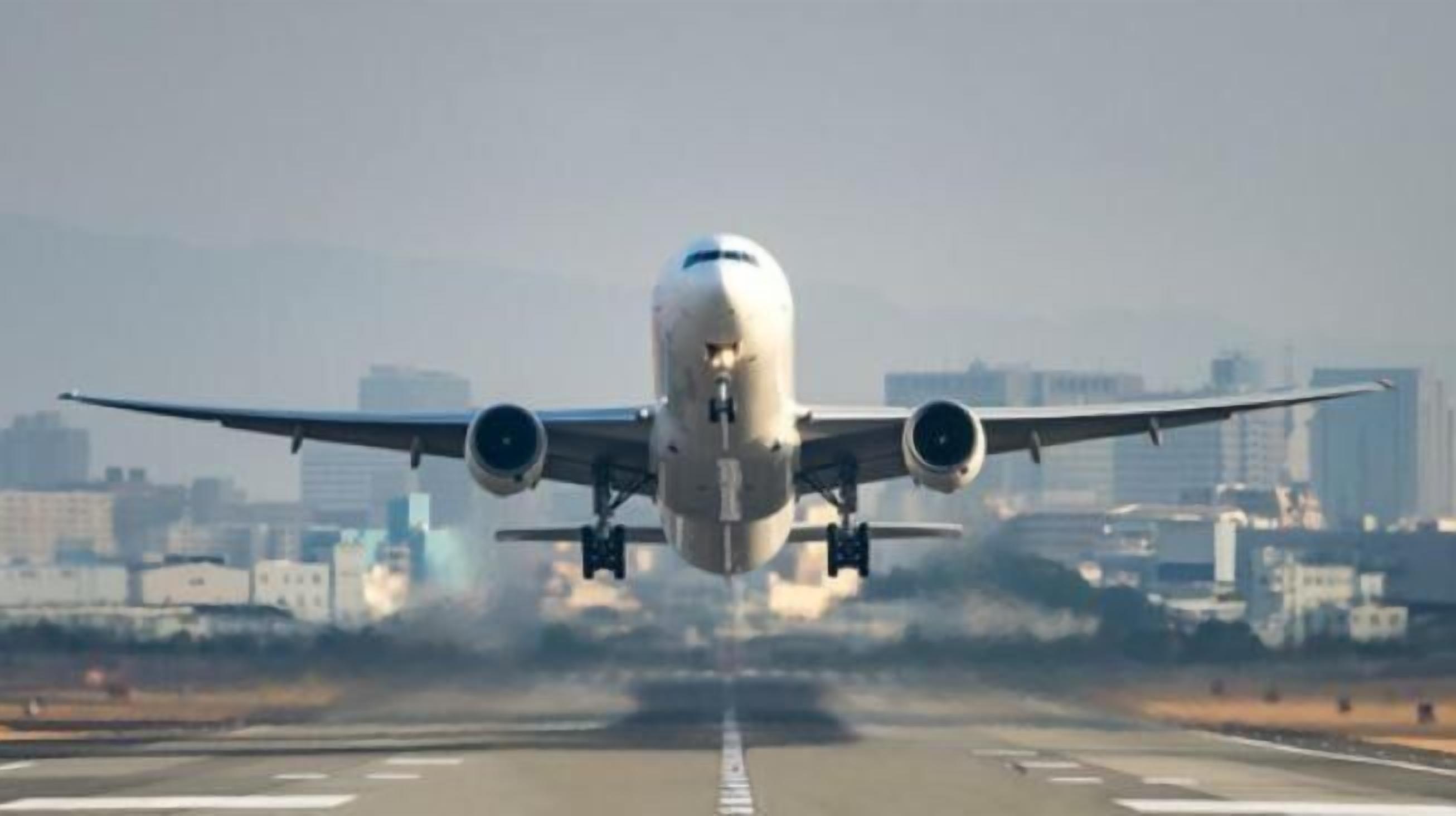 Un avión en la pista con edificios de la ciudad al fondo.