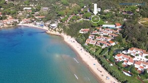 An aerial view of a coastal area with a beach, houses, and a pool. - Scaglieri Mare - ibookingelba.com (Portoferraio)