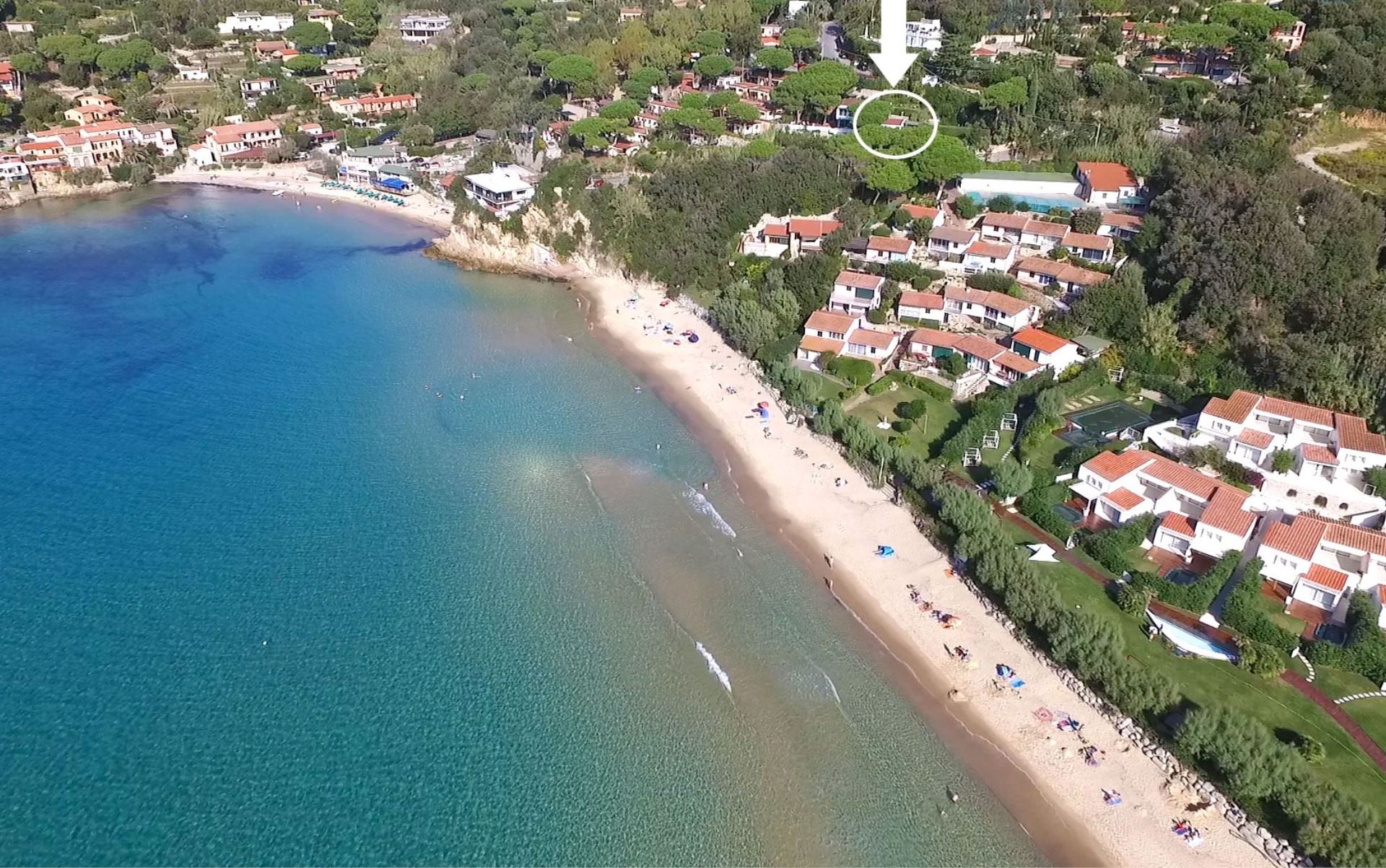 An aerial view of a coastal area with a beach, houses, and a pool.