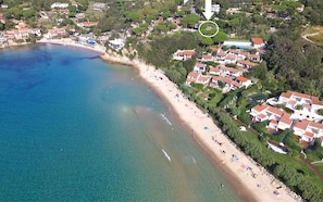 An aerial view of a coastal area with a beach, houses, and a pool.