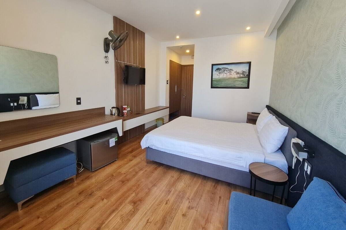 A modern hotel room with a bed, a desk, a chair, a small table, a TV, and a picture on the wall.