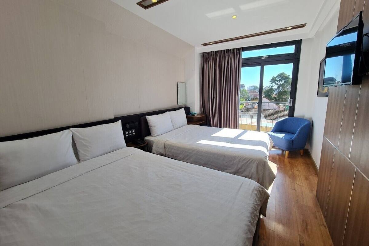A hotel room with two beds, a TV, a chair, and a large window with curtains.