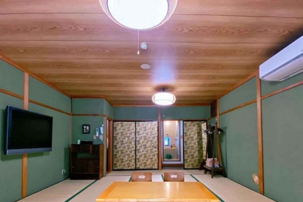 A traditional Japanese room with tatami flooring, a television, sliding doors, and a ceiling fan.