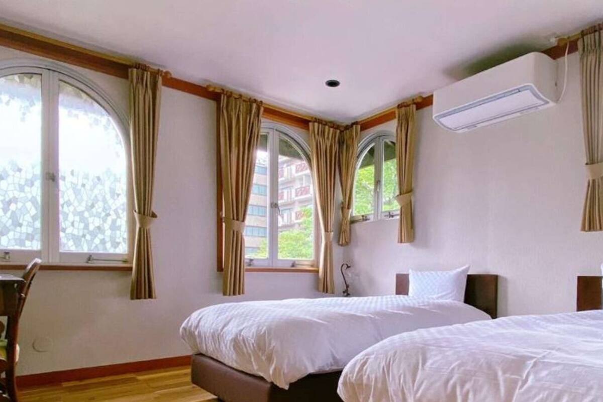 A hotel room with two beds, a desk, and large windows with curtains.