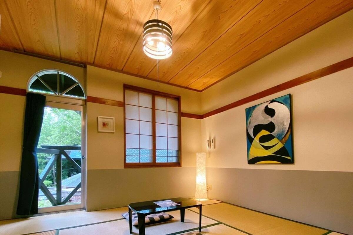 A traditional Japanese room with tatami flooring, a shoji screen door, a tatami mat table, and a painting on the wall.