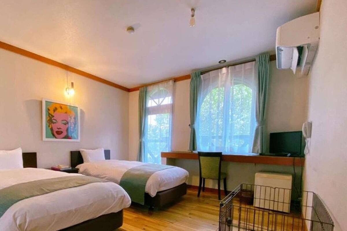 A hotel room with two beds, a desk with a chair, a television, and a window with curtains.