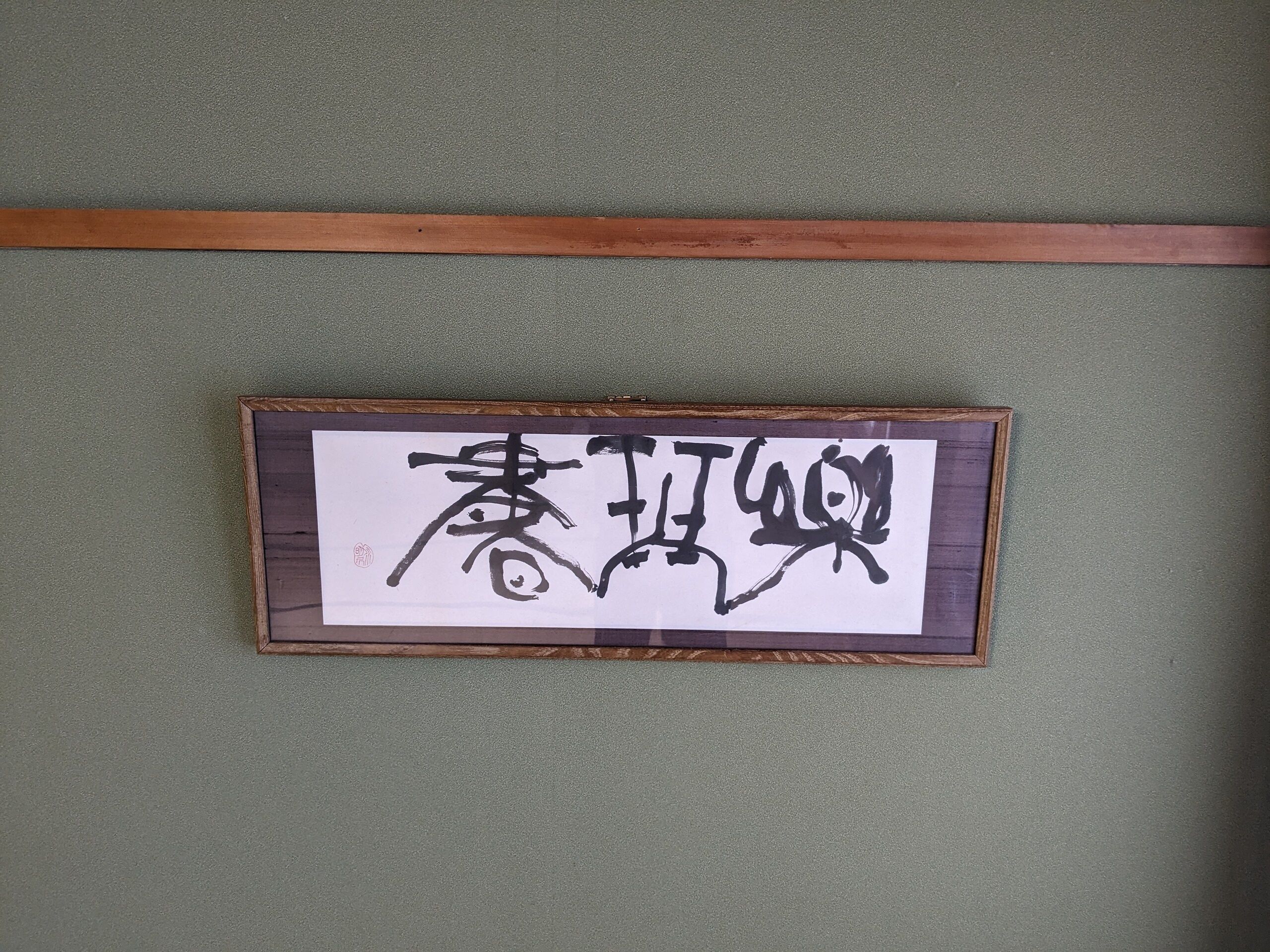 A framed calligraphy piece on a green wall.