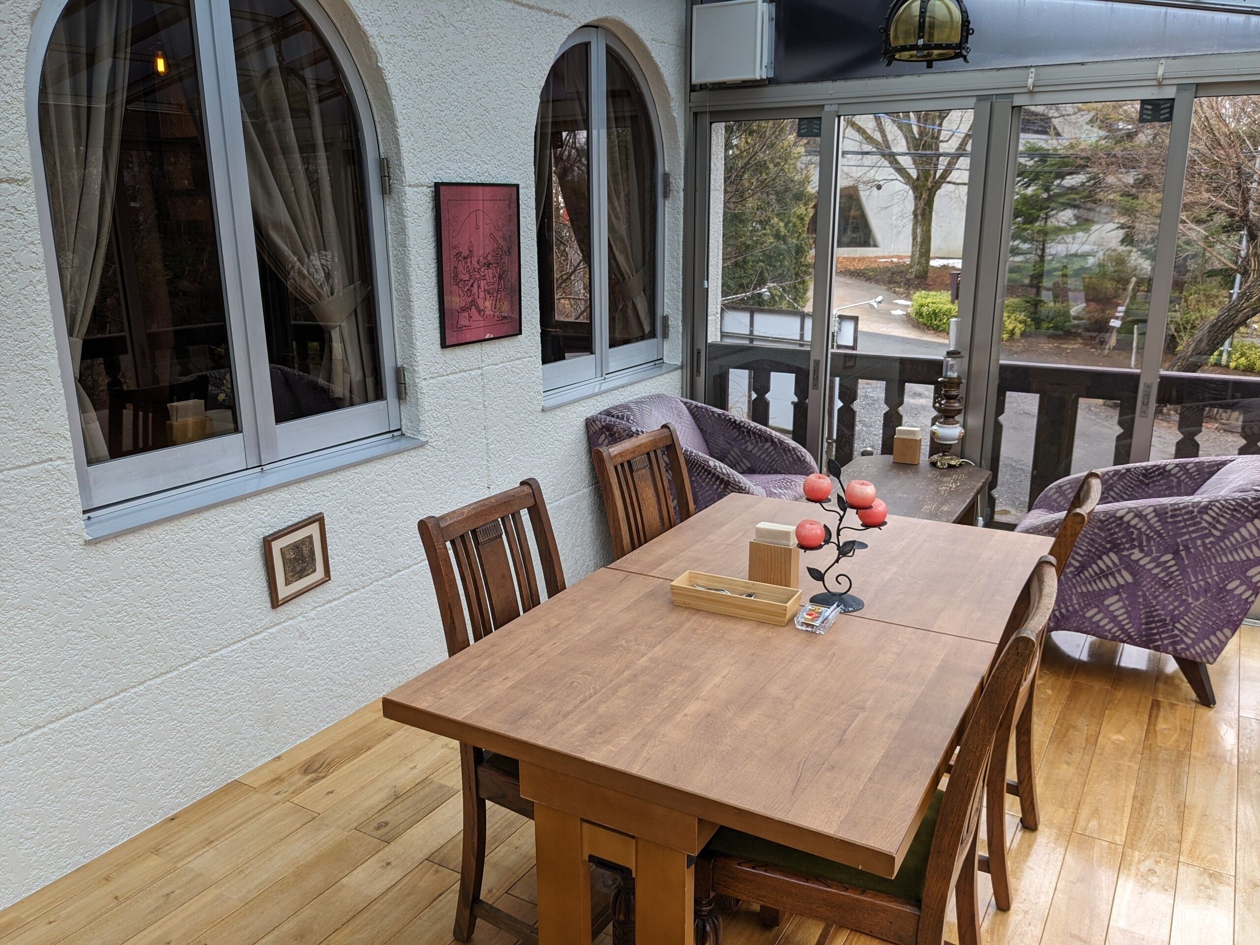 A wooden dining table with chairs, a glass door leading outside, and a small outdoor seating area with cushions.