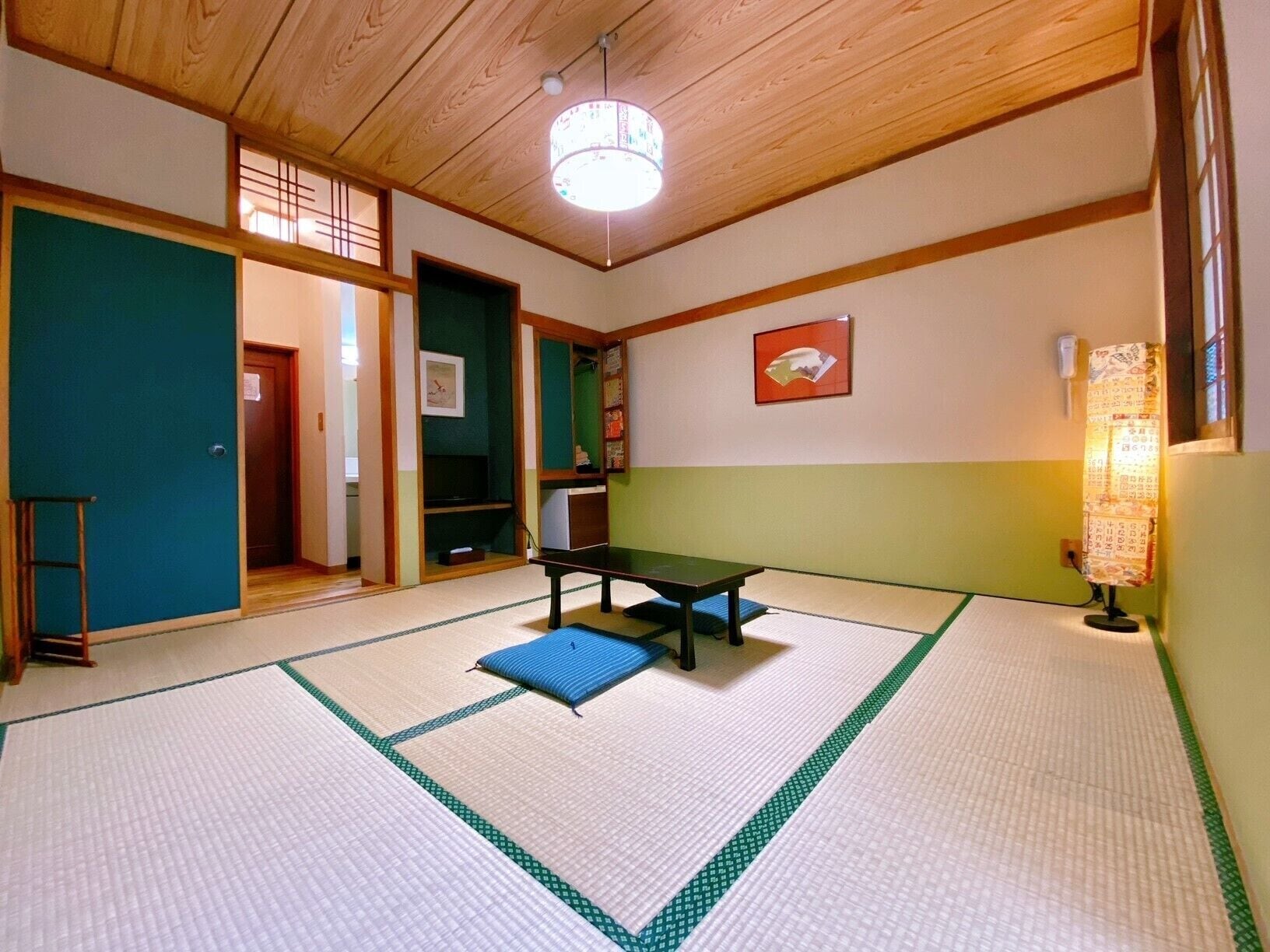 A tatami mat room with a low table and cushions, wooden beams on the ceiling, and a traditional Japanese paper lantern.