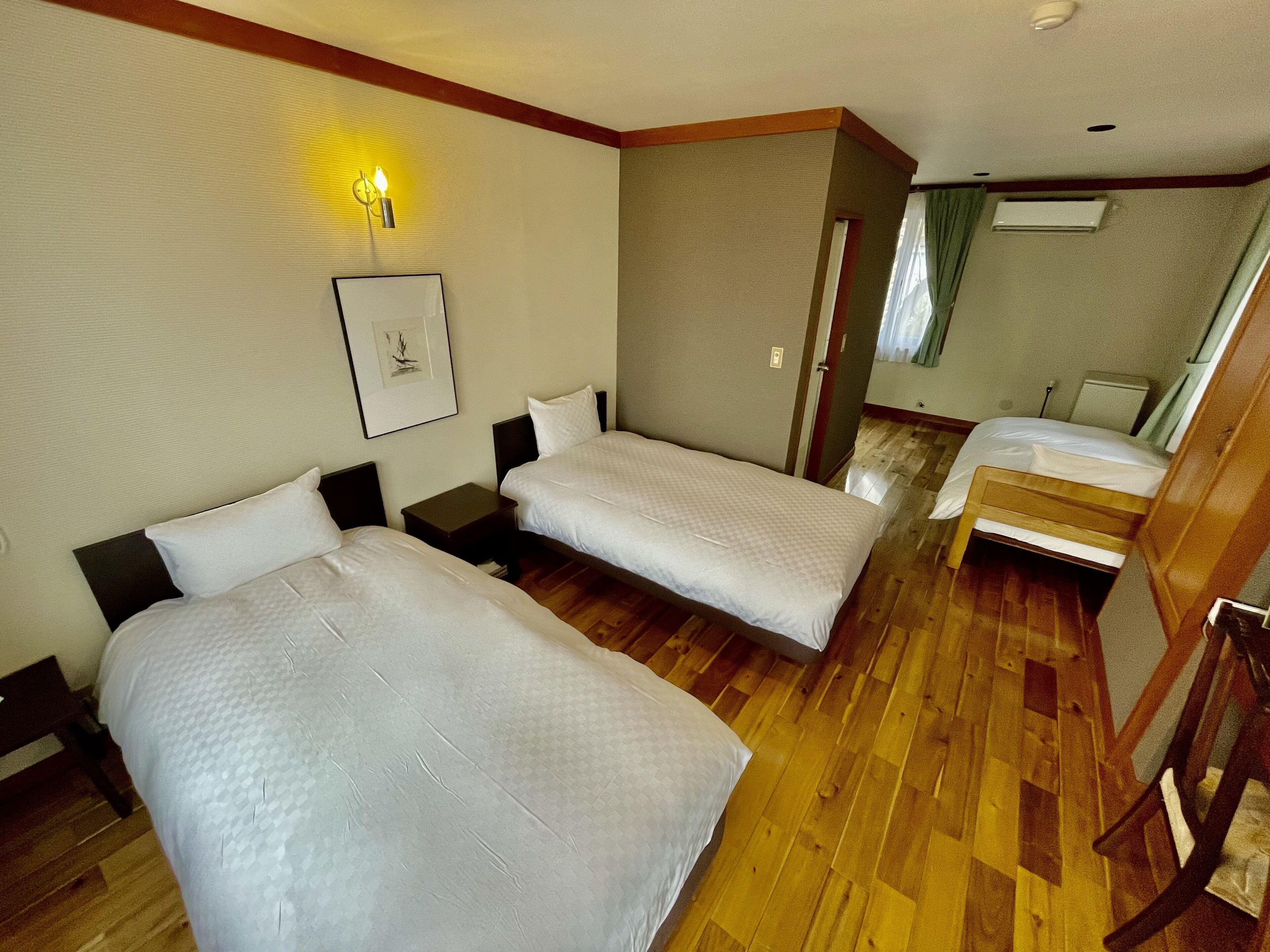 A hotel room with two single beds, a wooden floor, a framed picture on the wall, and a small table between the beds.