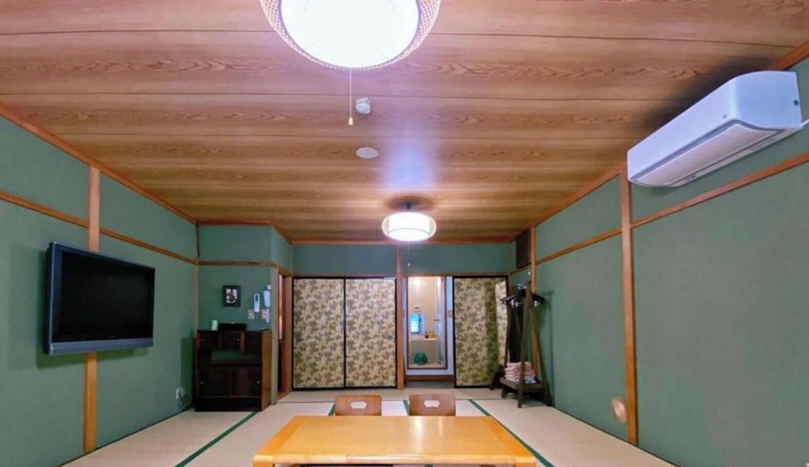 A traditional Japanese room with tatami flooring, a television, sliding doors, and a ceiling fan.