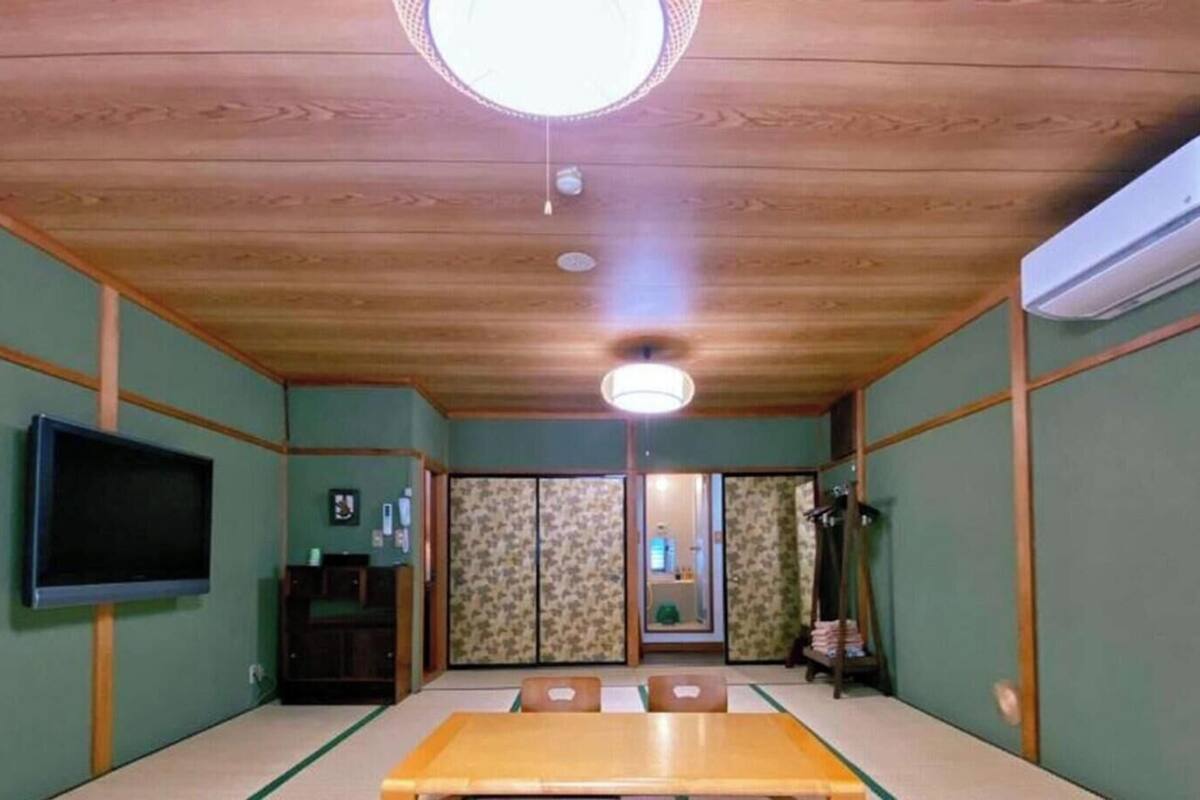 A traditional Japanese room with tatami flooring, a television, sliding doors, and a ceiling fan.