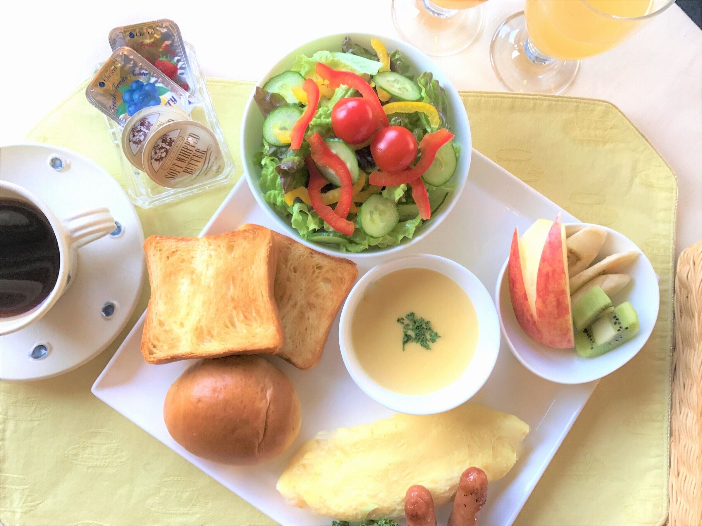A breakfast tray with toast, a bowl of salad, a cup of coffee, a bowl of soup, and a plate with fruit and sausages.