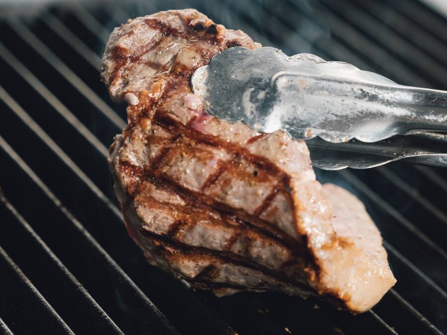 Un filete a la parrilla siendo volteado con pinzas.