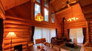 A log cabin interior with a dining table, chairs, a sofa, and a fireplace. - Lodge Atelier (Hokuto)