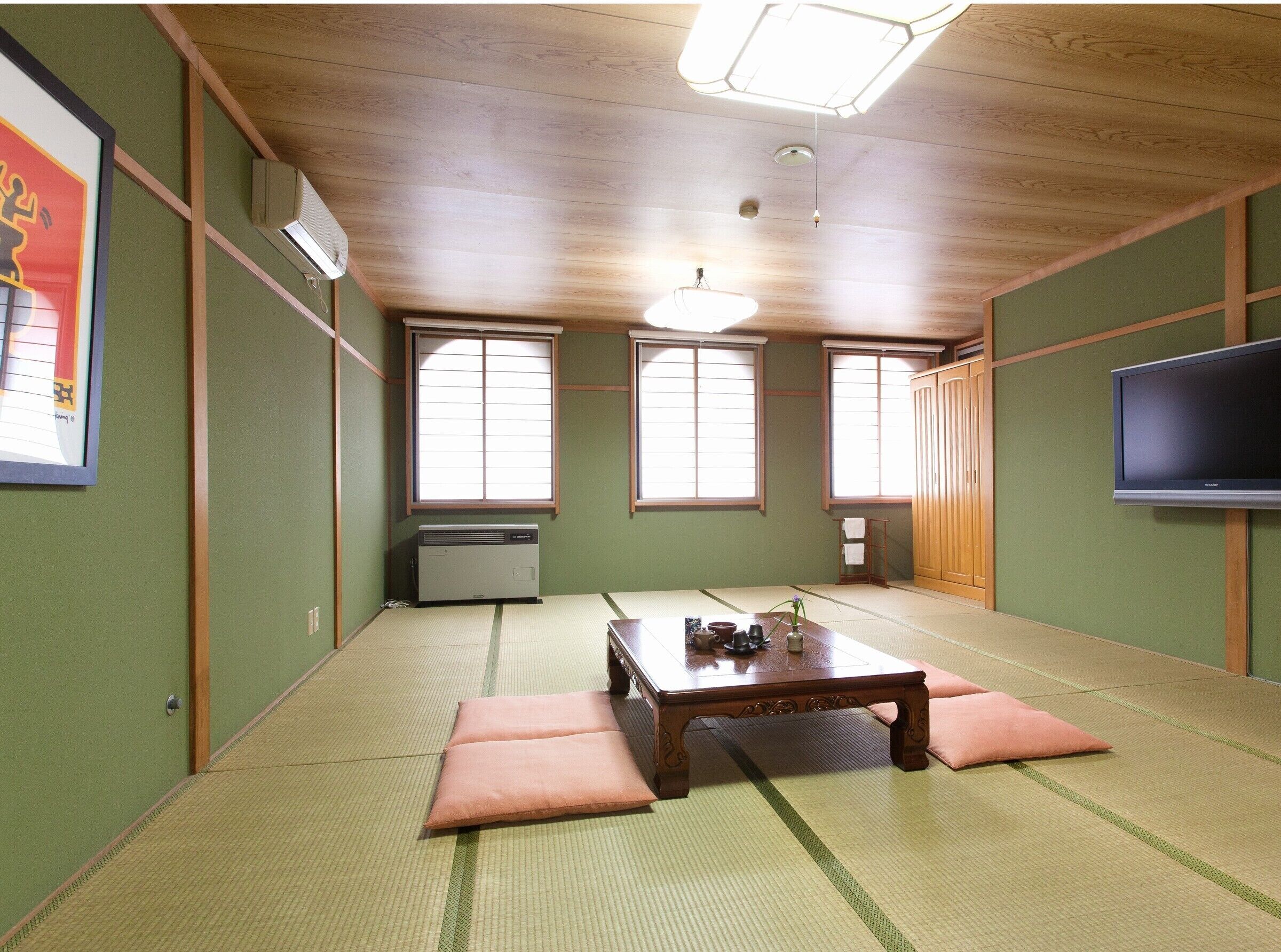 Una habitación tradicional japonesa con esteras de tatami, una mesa de madera, cojines, un televisor y puertas correderas.