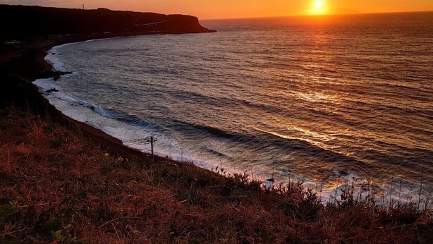 Vista de un atardecer costero con playa y acantilados.