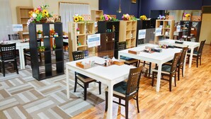 Un vestíbulo de hotel con varias mesas y sillas, pisos de madera y estanterías con flores y plantas.