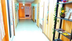 Un pasillo con paneles de madera, puertas, y un estante con cuadros enmarcados y plantas.