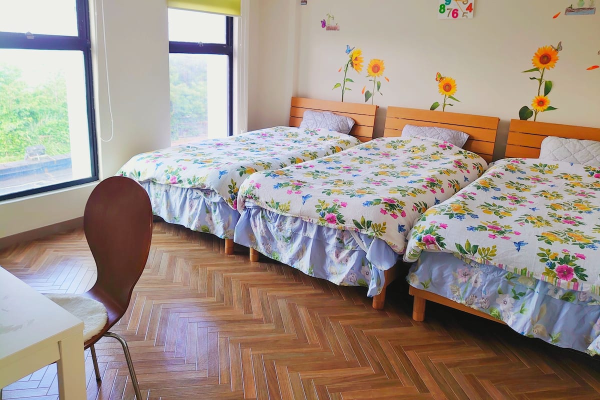 A room with two wooden beds, a wooden chair, and a window with a view of greenery.