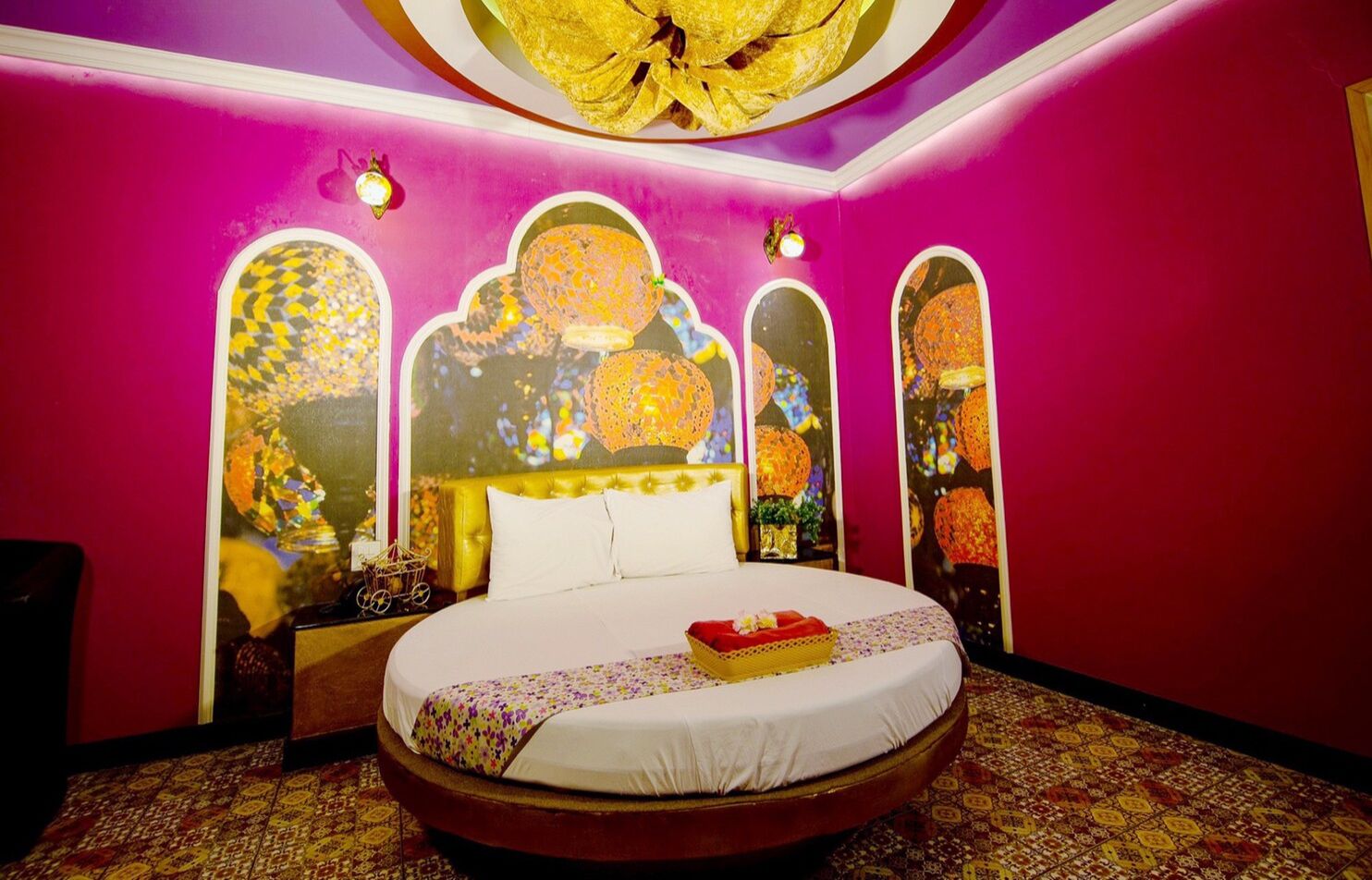 A room with a large round bed, pink walls, and decorative windows.