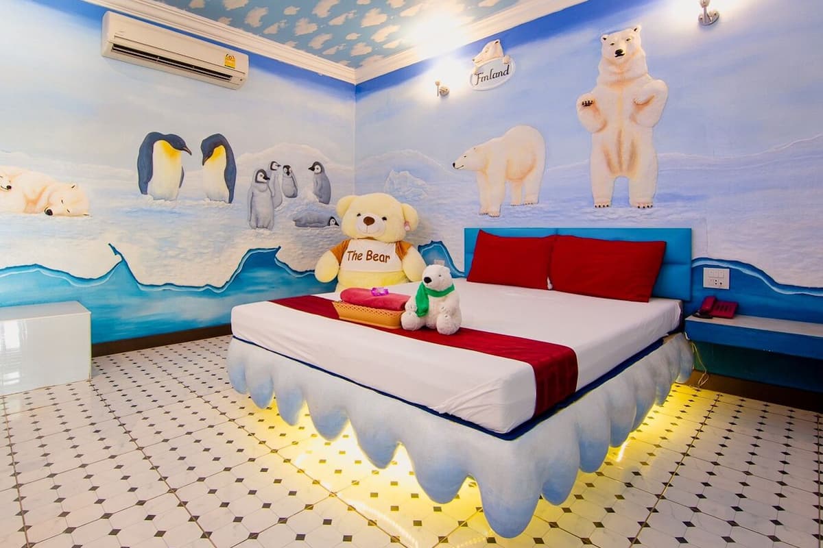 A room with a bed, a white chair, and a wall mural of polar bears and penguins.