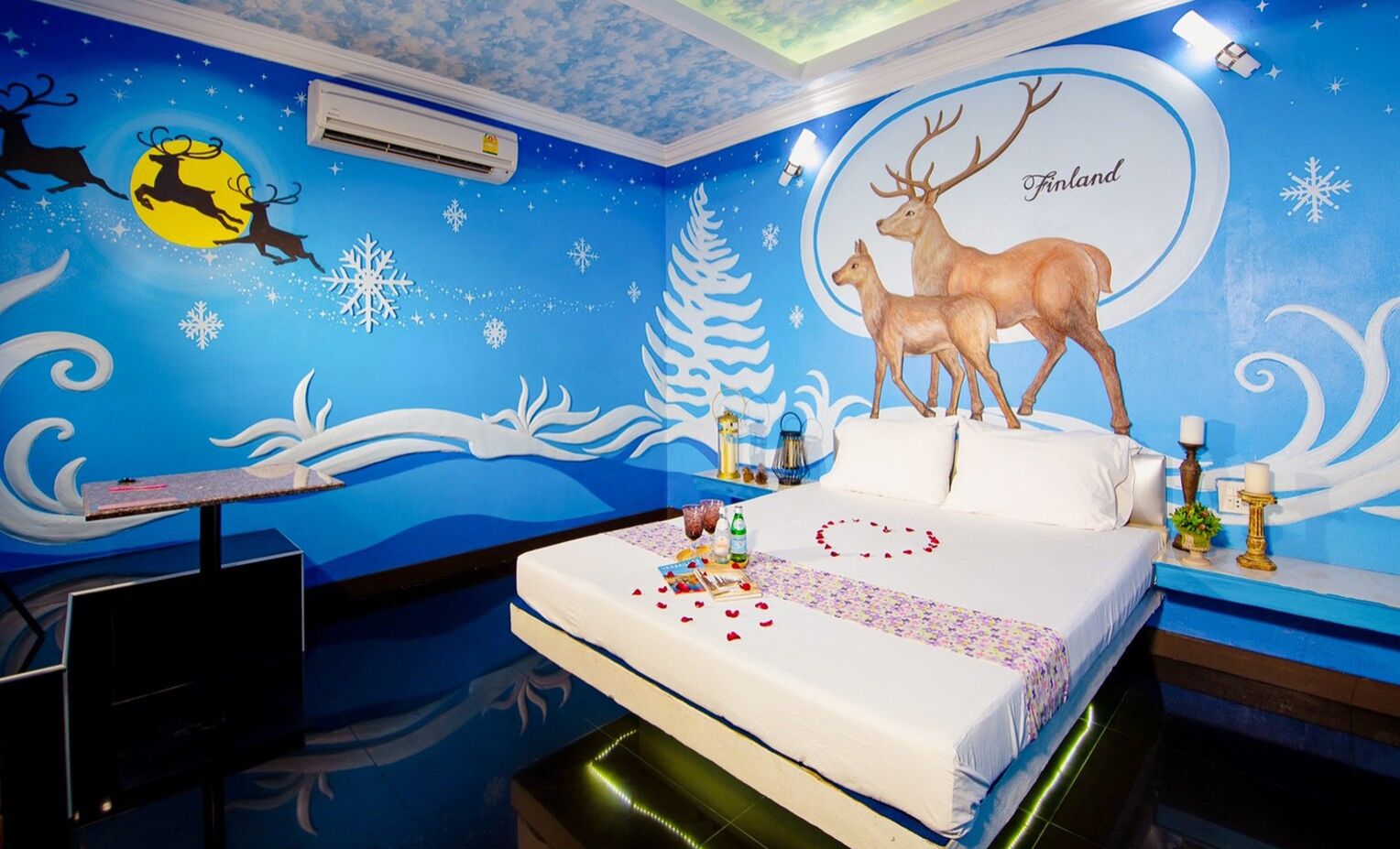 Habitación de hotel con cama, mesita de noche y un mural que muestra renos y copos de nieve.