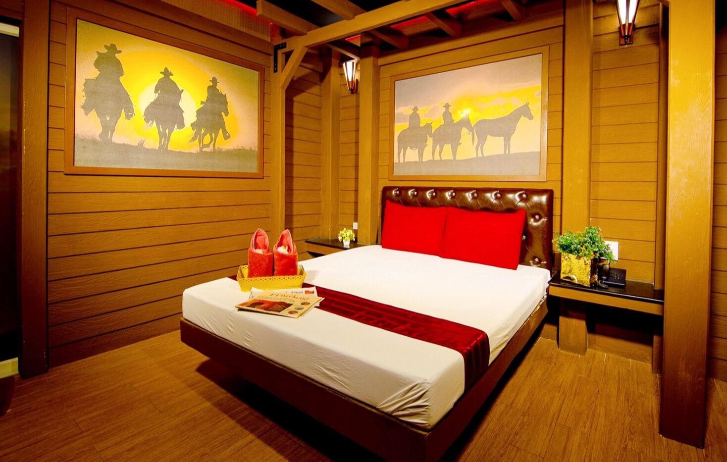 A hotel room with a large bed, wooden walls, and two paintings of cowboys on horseback.