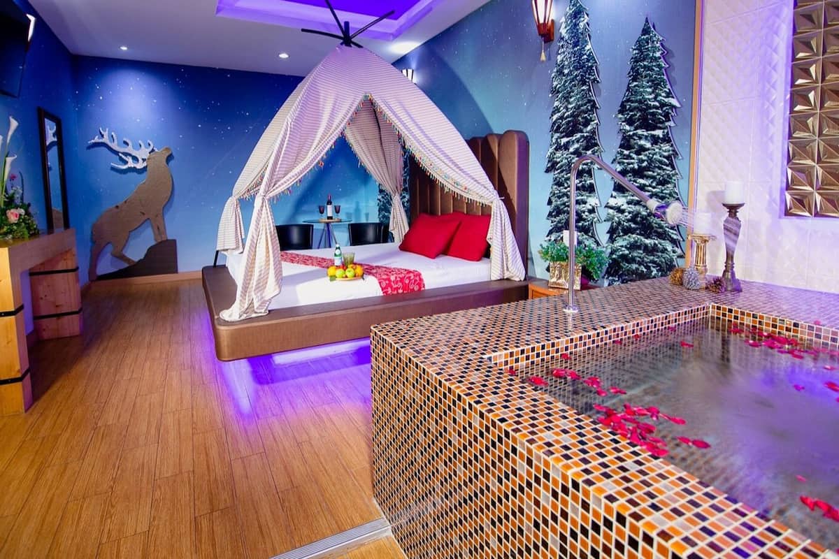 A cozy bedroom with a canopy bed, a small table with fruit, and a decorative fireplace.