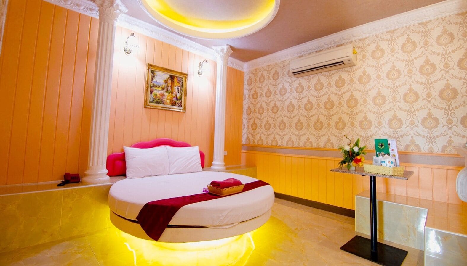 A hotel room with a bed, a small table with a vase, and a wall-mounted air conditioner.