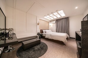 A modern hotel room with a bed, bedside table, lamp, and a desk with a chair.