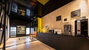 A modern hotel lobby with a reception desk, a coffee machine, and a refrigerator stocked with beverages.