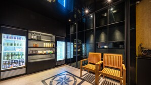 A bar area with a wooden bench, a refrigerator, and shelves stocked with beverages and snacks.