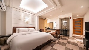 A hotel room with a large bed, a desk, a chair, a TV, and a bathroom with a mirror and sink.