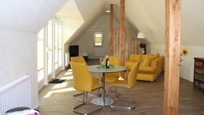 Un moderno salón con techo alto, una mesa redonda de vidrio con sillas amarillas, un sofá amarillo y una pared de acento de madera.