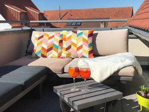 An outdoor seating area with a sofa, colorful pillows, a white towel, and two glasses of red drink on a wooden table. - Great, open loft apartment with fantastic roof terrace (Burgbernheim)