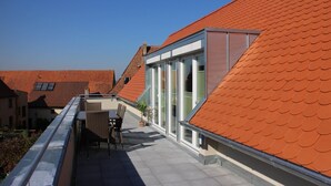 Terraza residencial en la azotea con comedor, plantas en macetas y vistas a edificios vecinos.