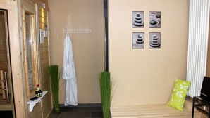 Un cuarto de spa con un banco de madera, un perchero, un estante en la pared con botellas y una planta verde.