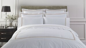 A neatly made bed with white bedding and gold trim, a bedside table with a lamp and flowers, and a green upholstered headboard. - Demiral Hotel at The Place Lekki (Lekki)