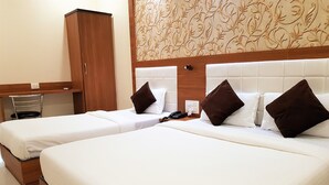 A hotel room with two single beds, a wooden wardrobe, a small table with a chair, and a patterned wall. - Hexa Royal Elite (Mumbai)