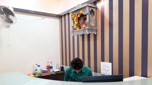 A reception desk with a glass top, a wall-mounted fan, and a decorative shelf with flowers. - Hexa Royal Elite (Mumbai)