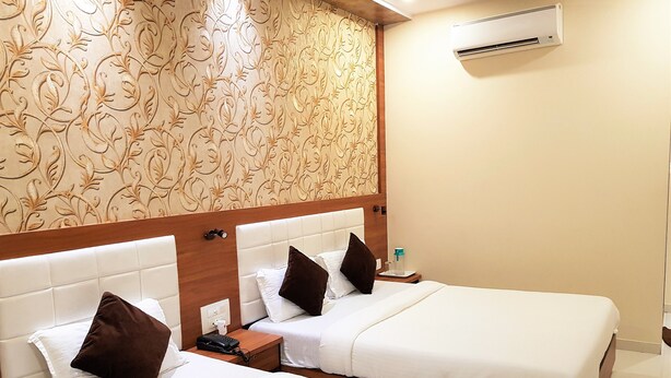A hotel room with two beds, a wooden headboard, a wall air conditioner, and a patterned wallpaper. - Hexa Royal Elite (Mumbai)