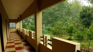 A corridor with checkered flooring and wooden railings, leading to a balcony with a view of a lush green landscape. - Ack Palacce Inn (Yercaud)