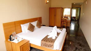 A hotel room with a large bed, wooden headboard, a nightstand with a kettle, and a wardrobe. - Ack Palacce Inn (Yercaud)