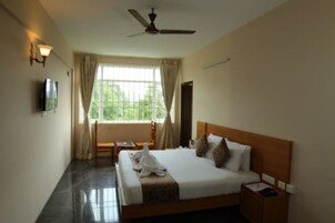 Una habitación de hotel con cama, escritorio, silla, televisor y ventana con cortinas.